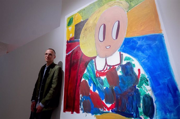 El artista André Butzer posa junto a una obra de su primera retrospectiva en una institución fuera de su país, en el Museo Nacional Thyssen-Bornemisza, a 8 de mayo de 2023, en Madrid (España). 