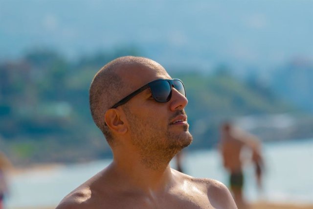 Archivo - Hombre con calva y gafas toma el sol en la playa.