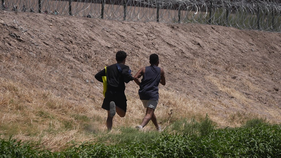 11 May 2023, Mexico, Tijuana: Two young migrants from Venezuela walk along the Rio Bravo River near the barbed wire fence between Mexico and the US. 