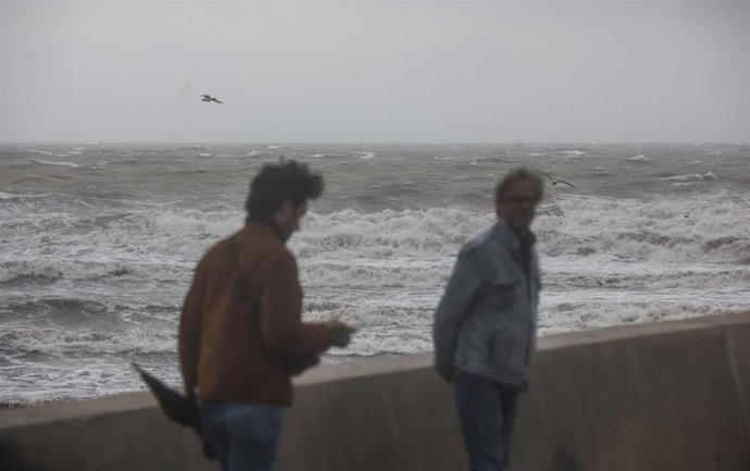 Archivo - Dos personas caminan en la playa un día de fuerte viento 