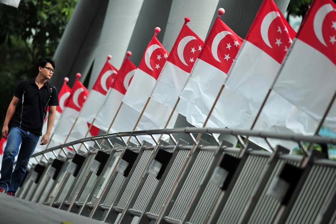 Archivo - Un hombre camina en Singapur junto a varias banderas del país