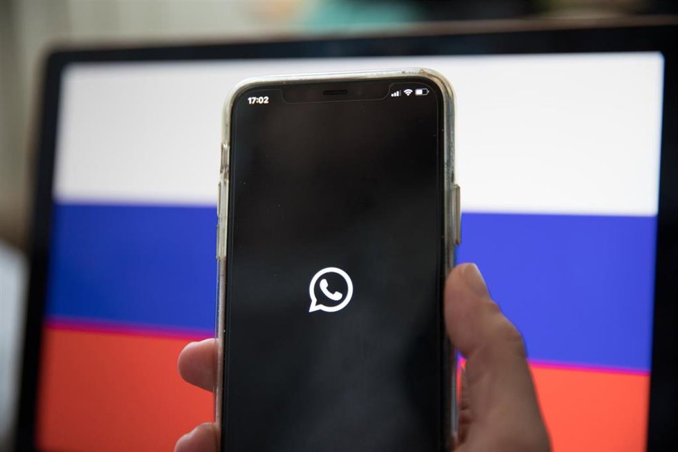 Archivo - Imagen de archivo de un móvil con la aplicación de mensajería WhatsApp frente a un ordenador con la bandera de Rusia