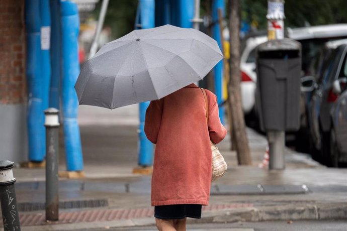 Una mujer pasea por una calle con un paraguas