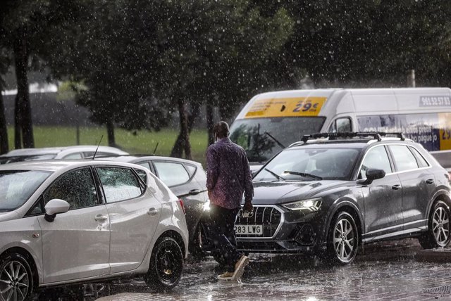 Archivo - Un hombre camina entre varios coches mientras la lluvia cae en imagen de archivo
