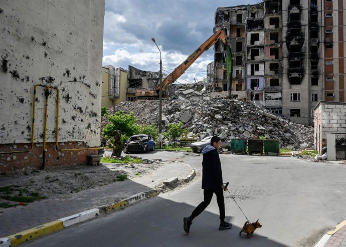 13 May 2023, Ukraine, Irpin: A resident walks with a dog near badly damaged apartment buildings that were hit during the Russian invasion of Ukraine. Photo: Sergei Chuzavkov/SOPA Images via ZUMA Press Wire/dpa