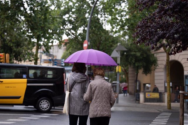 Varias personas con paraguas pasean por una de las calles de Barcelona.