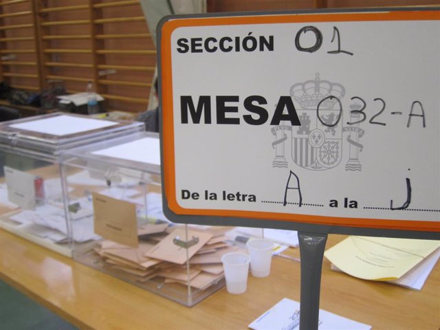 Archivo - Cartel de una mesa electoral con las urnas al fondo