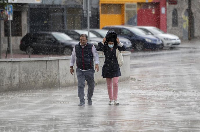 Dos personas bajo la lluvia antes de la celebración del acto de cierre de campaña del PSOE Madrid, en el Centro Cultural Antonio López, a 26 de mayo de 2023, en Coslada, Madrid (España).
