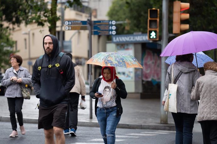 Varias personas con paraguas pasean por una de las calles de la ciudad, a 12 de mayo de 2023, en Barcelona, Catalunya (España). 