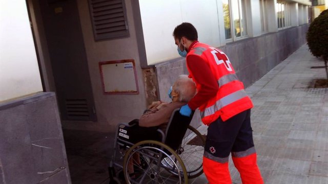 Un trabajador de Cruz Roja ayuda a una mujer mayor en silla de ruedas.