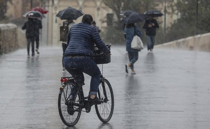 Archivo - Una persona circula en bicicleta bajo la lluvia en imagen de archivo