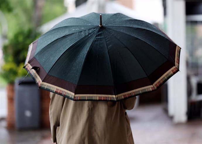 Archivo - Una persona camina con paraguas para protegerse de la lluvia.