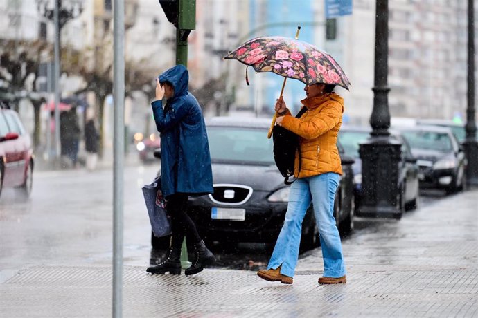 Archivo - Dos personas con paraguas pasan por un paso de cebra.- Archivo