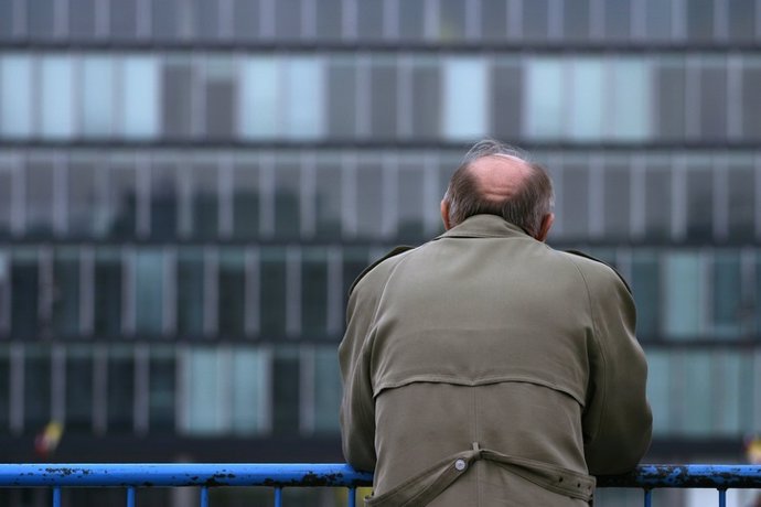 Archivo - Bald man in brown standing alone against a blue railing