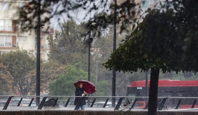 Archivo - Una dona camina mentre es protegeix de la pluja amb un paraigua en imatge d'arxiu