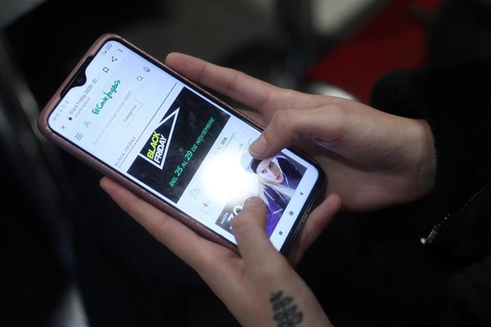 Archivo - Una joven consulta las ofertas en su móvil
