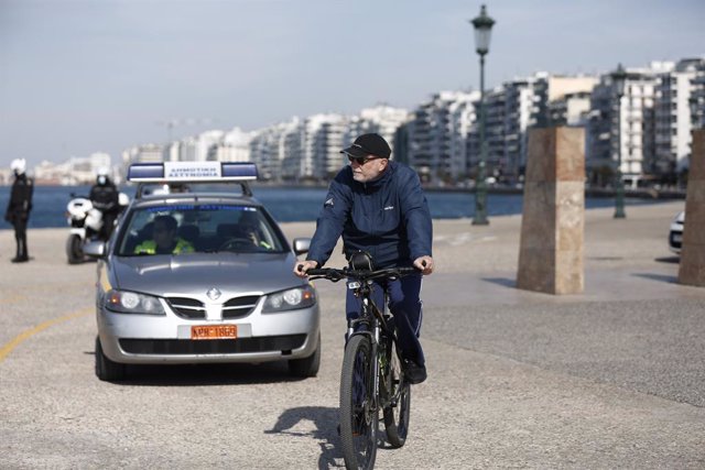 Archivo - March 18, 2020, Thessaloniki, Greece: A man rides a bicycle in front of a Municipality Police Car. Greek police and Municipality Police of Thessaloniki patrols at the waterfront of the city, urging the citizens to stay in their homes due to the 