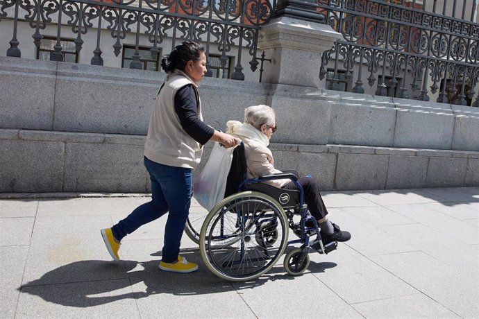 Una mujer mayor en silla de ruedas y su cuidadora pasean por el centro de la ciudad, a 4 de junio de 2023, en Madrid (España). 