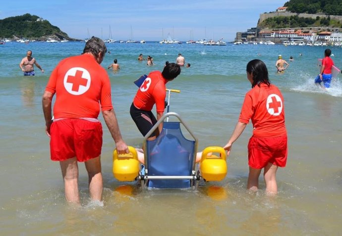 Archivo - Voluntarios de Cruz Roja asisten en la playa a una persona con movilidad reducida