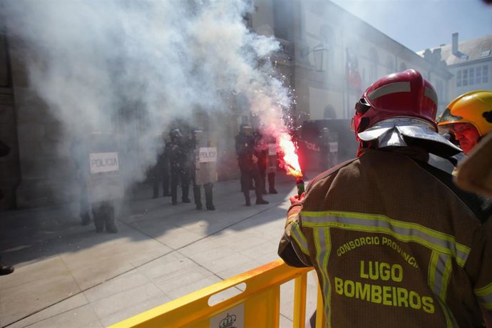 Un bombero de consorcios provinciales sujeta una bengala de humo de color durante una protesta ante la sede de la Xunta, a 23 de mayo de 2023, en Lugo, Galicia (España). Los bomberos de consorcios provinciales se manifiestan en Lugo en defensa de mejora