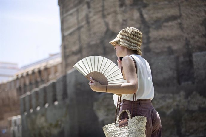 Una mujer se protege del sol con sombrero y abanico.