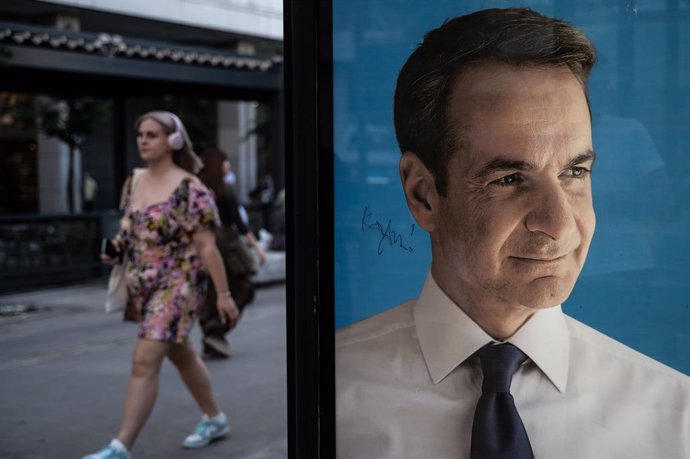 21 June 2023, Greece, Athens: A woman walks past an election poster of party leader Kyriakos Mitsotakis of the conservative New Democracy party in the center of the Greek capital. Greeks will elect a new parliament on June 25. Photo: Angelos Tzortzinis/