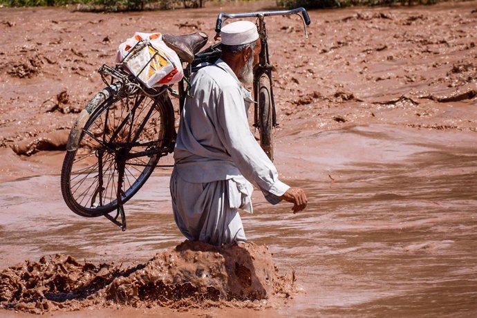 Archivo - 15 April 2020, Pakistan, Peshawar: A man holds his bike as he wades through muddy floodwatrs to cross a bridge above the Bara River following heavy rains in Peshawar. Photo: Hasnain Ali/IMAGESLIVE via ZUMA Wire/dpa