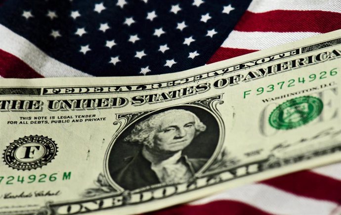 Archivo - Billete de dólar y bandera de Estados Unidos.