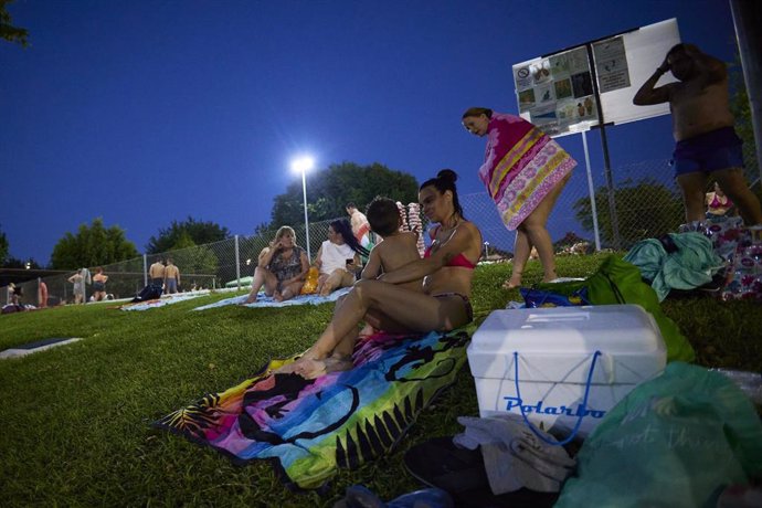 Una familia en el césped de la piscina municipal de Gines, a 26 de junio de 2023 en Sevilla (Andalucía, España). El Ayuntamiento de Gines ha abierto este lunes desde las 21,30 hasta las 00,30 horas la piscina municipal para combatir la intensa ola de ca