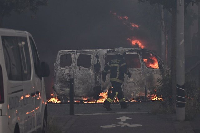 28 June 2023, France, Toulouse: A firefighter walks past a burning vehicle as riots and protests break out. Protests erupted again in several French cities on Wednesday evening after a police officer fatally shot a 17-year-old during a traffic stop near P