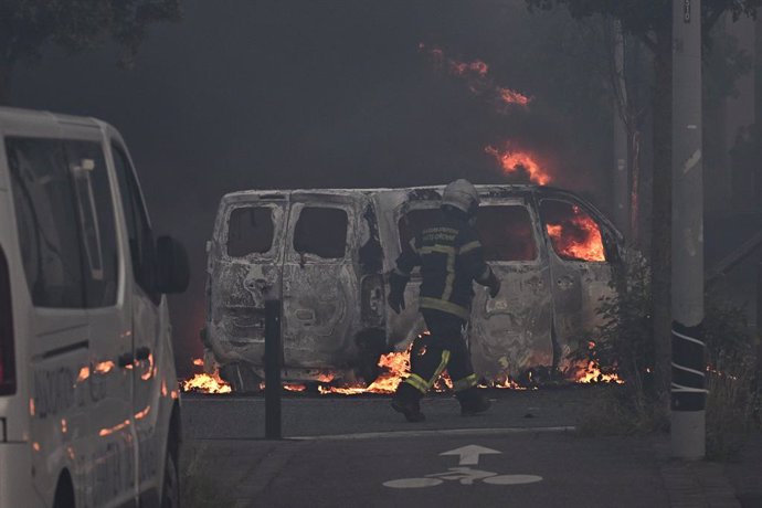 28 June 2023, France, Toulouse: A firefighter walks past a burning vehicle as riots and protests break out. Protests erupted again in several French cities on Wednesday evening after a police officer fatally shot a 17-year-old during a traffic stop near