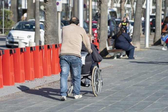 Archivo - Una persona acompañando a otra en silla de ruedas.