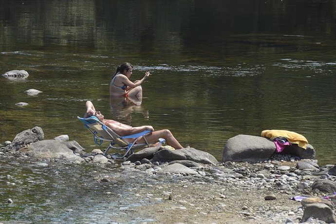 Archivo - Dos personas se remojan en la orilla de un río.