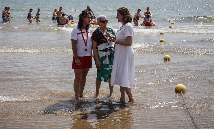 La alcaldesa de Valncia, María José Catalá, junto a una representante de Cruz Roja y una usuaria durante la presentación de la temporada de playas 2023 en la ciudad. Playa de El Cabanyal. 