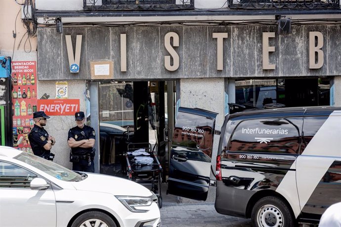 Dos agentes de Policía Nacional y el vehículo de Interfunerarias antes de trasladar el cuerpo de la mujer apuñalada en la tienda de ropa de trabajo Vistebien, en la plaza de Tirso de Molina, a 3 de julio de 2023, en Madrid (España). 