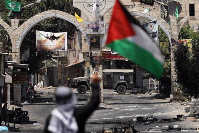 Un hombre agita la bandera palestina ante un vehículo militar de Israel