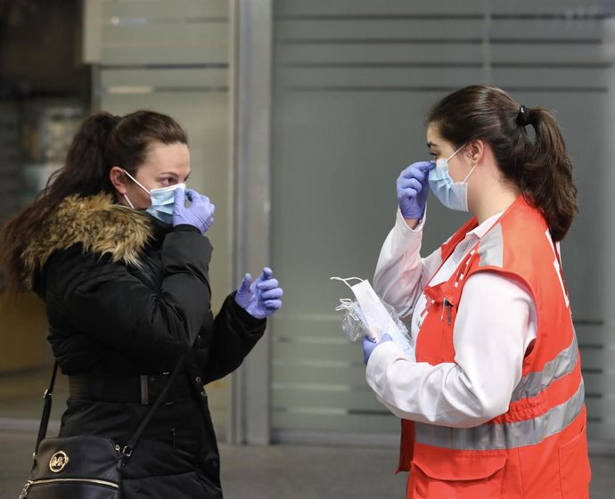 Archivo - Una voluntaria de Cruz Roja da indicaciones a una pasajera sobre cómo ponerse una mascarilla en la estación de Cercanías de Atocha durante el segundo día de reparto de mascarillas en el transporte público por la reactivación de la actividad la