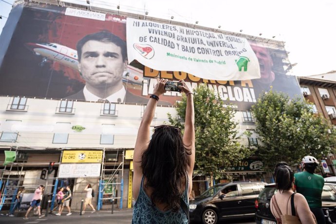Una mujer fotografía la nueva lona desplegada por el Movimiento de Vivienda de Madrid encima del cartel de Desokupa, donde se lee Ni alquileres, ni hipotecas, ni deudas. Vivienda gratuita, universal, de calidad y bajo control obrero.
