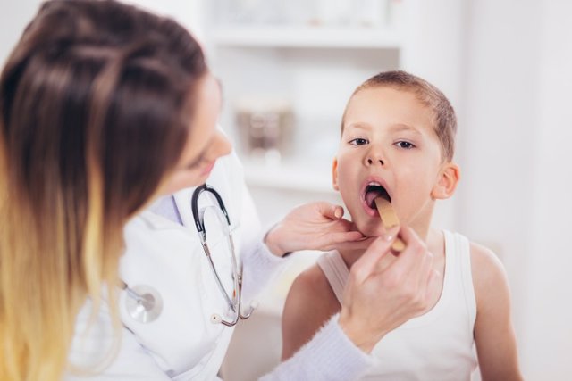 Archivo - Female doctor examining child with tongue depressor at surgery