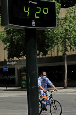 Archivo - Un hombre pasea en bicicleta junto un termómetro que marca 42 durante un día de alerta roja por altas temperaturas (foto de archivo)