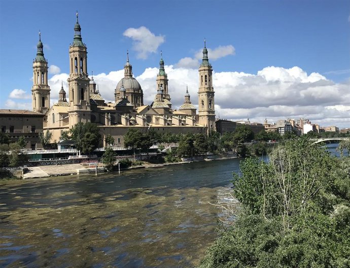 Río Ebro con poco caudal en el que se aprecian los macrófitos y mejanas con el Pilar al fondo