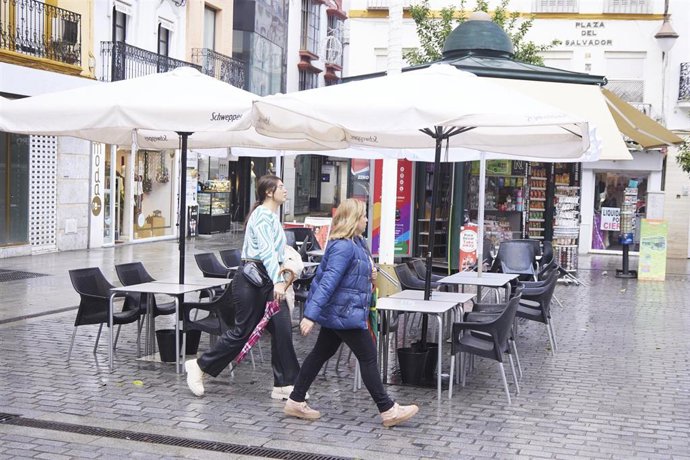 Archivo - Dos mujeres pasean por el centro de Sevilla antes veladores vacíos en una imagen de archivo.