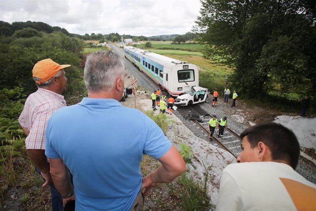Varias personas observan las consecuencias del choque del tren a un coche en un paso a nivel, a 12 de julio de 2023, en Lugo, Galicia (España). Un tren ha arrollado hoy a un coche con tres ocupantes en un paso a nivel sin barreras en la parroquia de Recim