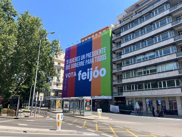 Lona del PP en Castellana, 60 con un fondo con los colores de varias formaciones políticas