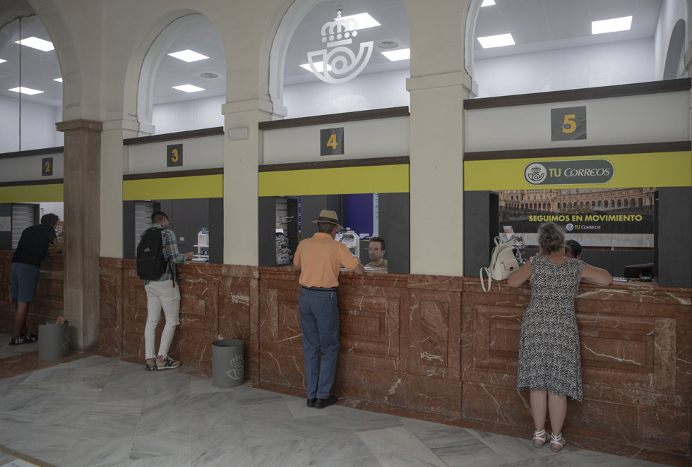 Varias personas en los mostradores de la oficina de Correos de la Avd. de la Constitución. A 19 de julio de 2023, en Sevilla (Andalucía, España).
