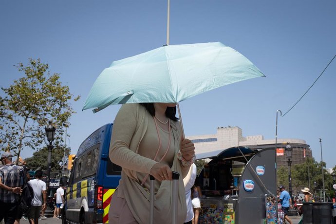 Una persona mira de protegir-se del sol a les Rambles, a Barcelona (Catalunya)