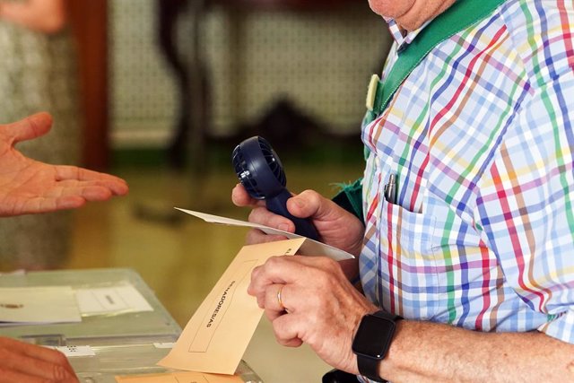 Una persona amb un ventilador portàtil en una mesa electoral