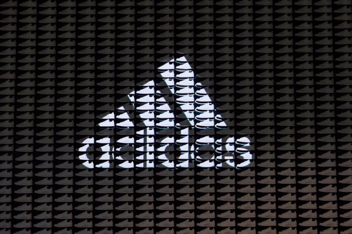 Archivo - FILED - 08 March 2023, Bavaria, Herzogenaurach: The logo with lettering of the sporting goods manufacturer adidas AG is projected onto a wall consisting of sneakers on the sidelines of the company's annual press conference. 