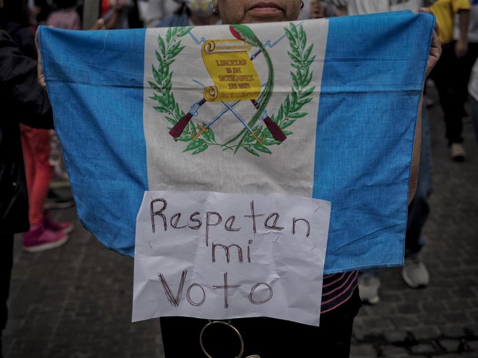 Bandera de Guatemala junto a un cartel en protesta por la situación electoral en el país
