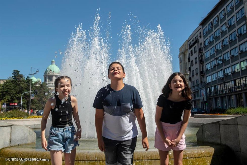 Tres niños se mojan en una fuente.
